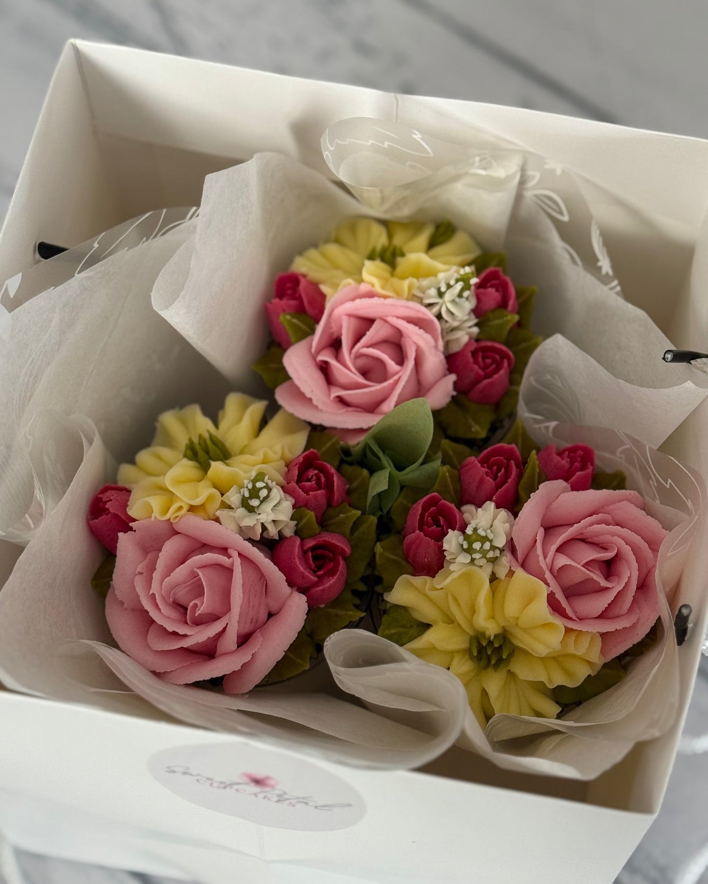 Bouquet of pink, yellow, and red flowers in a white box with tissue paper.