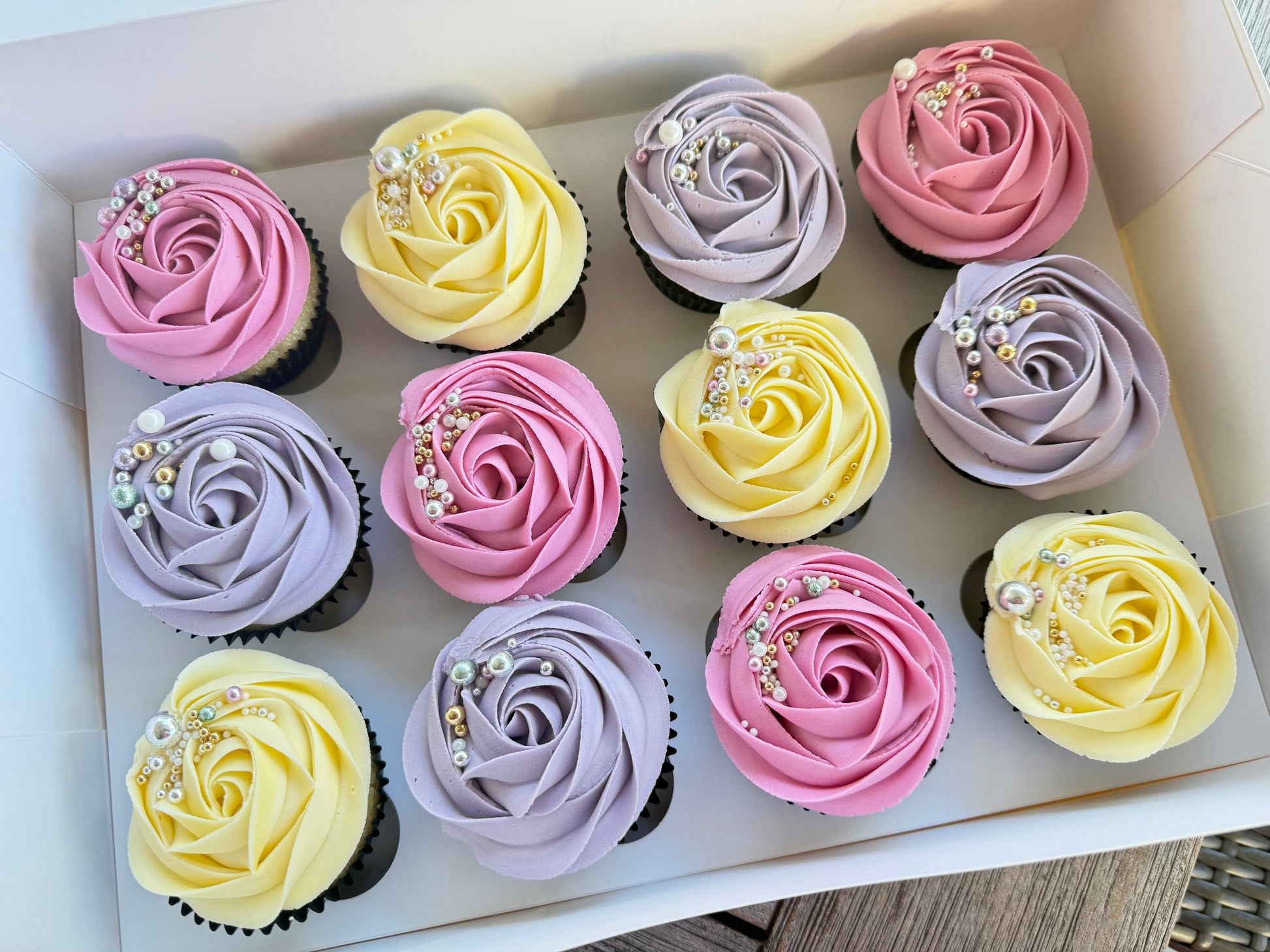 Box of cupcakes with pink, yellow, and purple buttercream