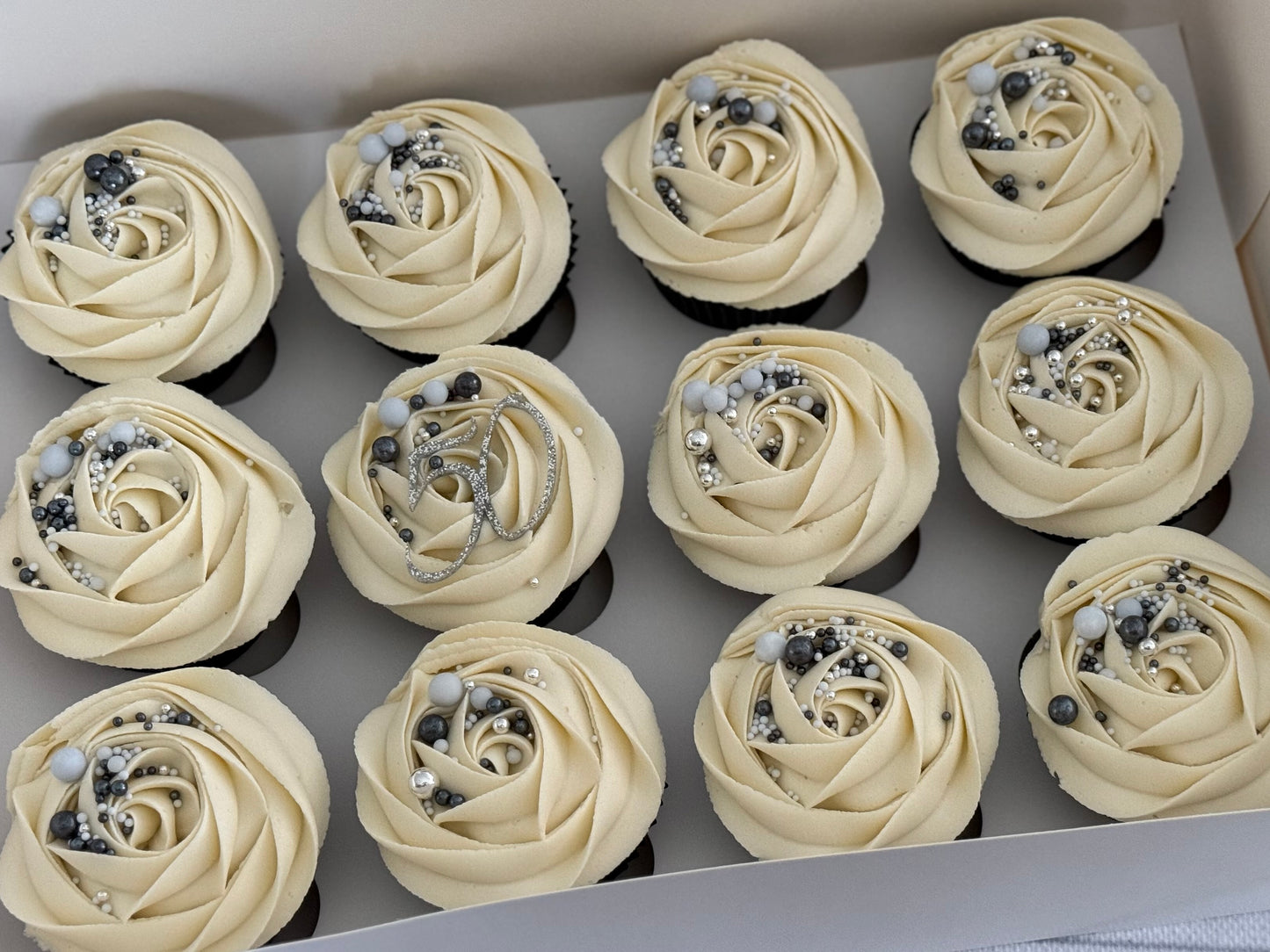 Cupcakes with white buttercream, sprinkles and topper arranged in a box.